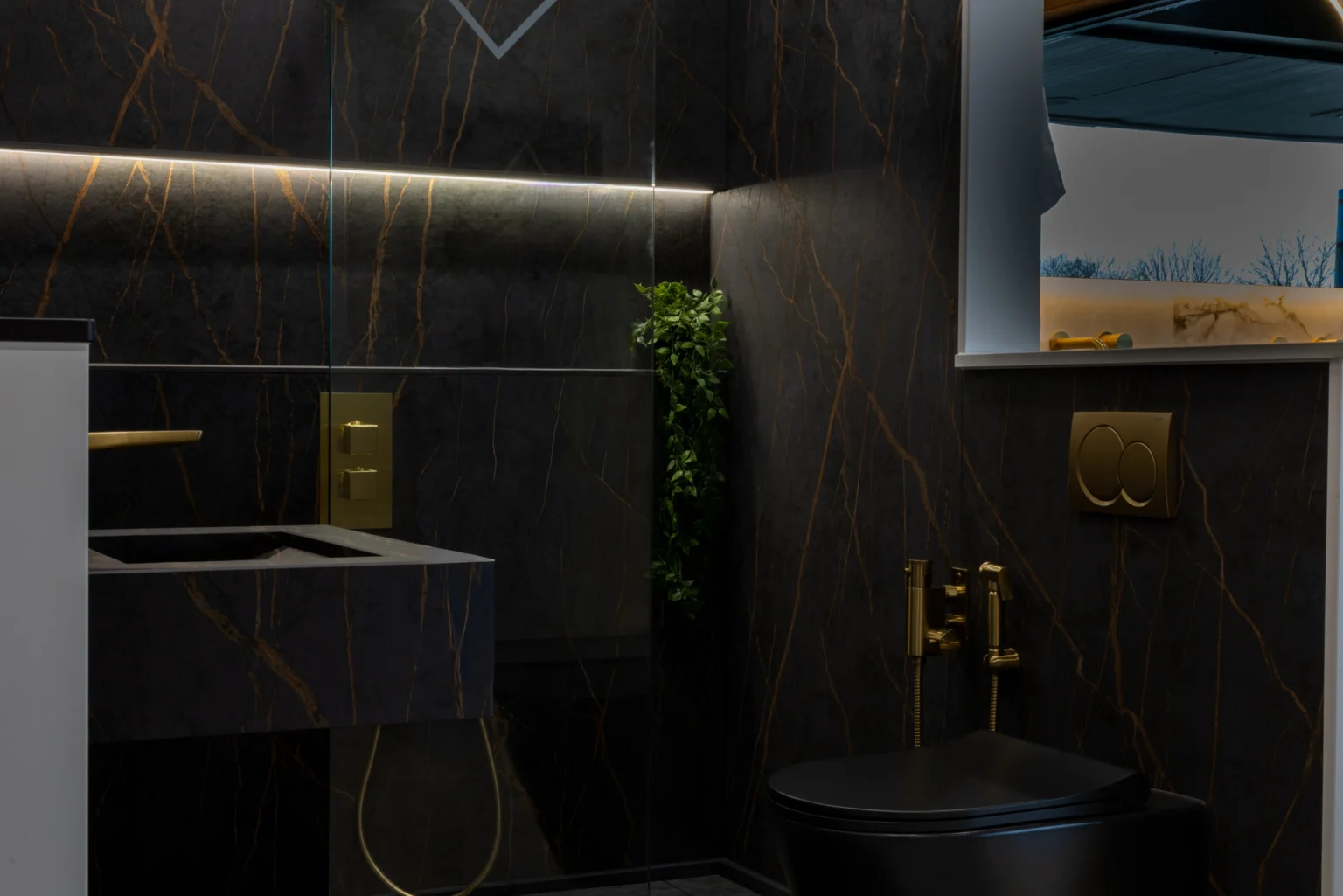 Dark marble-effect bathroom walls veined in gold, with a brushed brass shower valve and flush plate