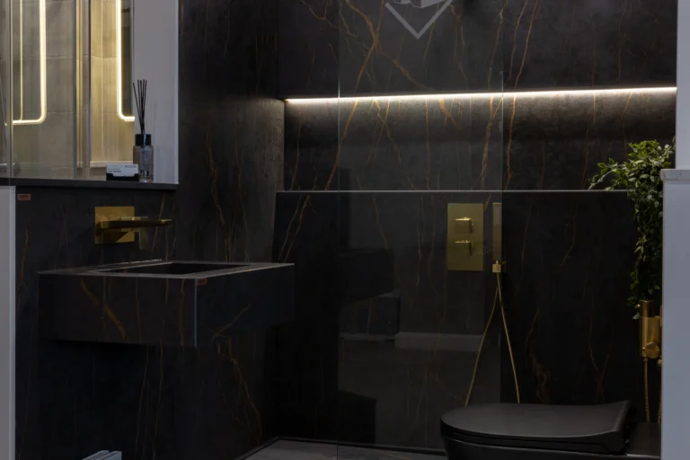 Black marble-effect walls veined in gold around a floating basin, a brushed brass shower valve and a black wall-hung toilet