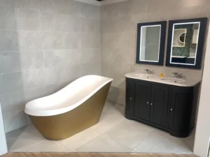 Showroom bathroom featuring large white marble-effect wall and floor tiles with gold freestanding bath