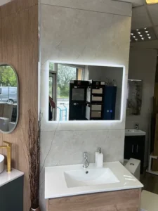 Showroom bathroom with ivory stone-effect wall tiles behind a lit mirror and basin