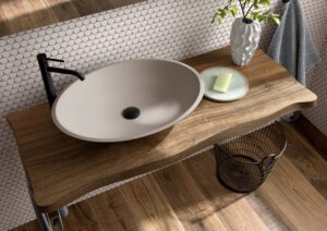 Oval stone resin vessel basin on a live-edge walnut shelf with black tap and penny mosaic tiles