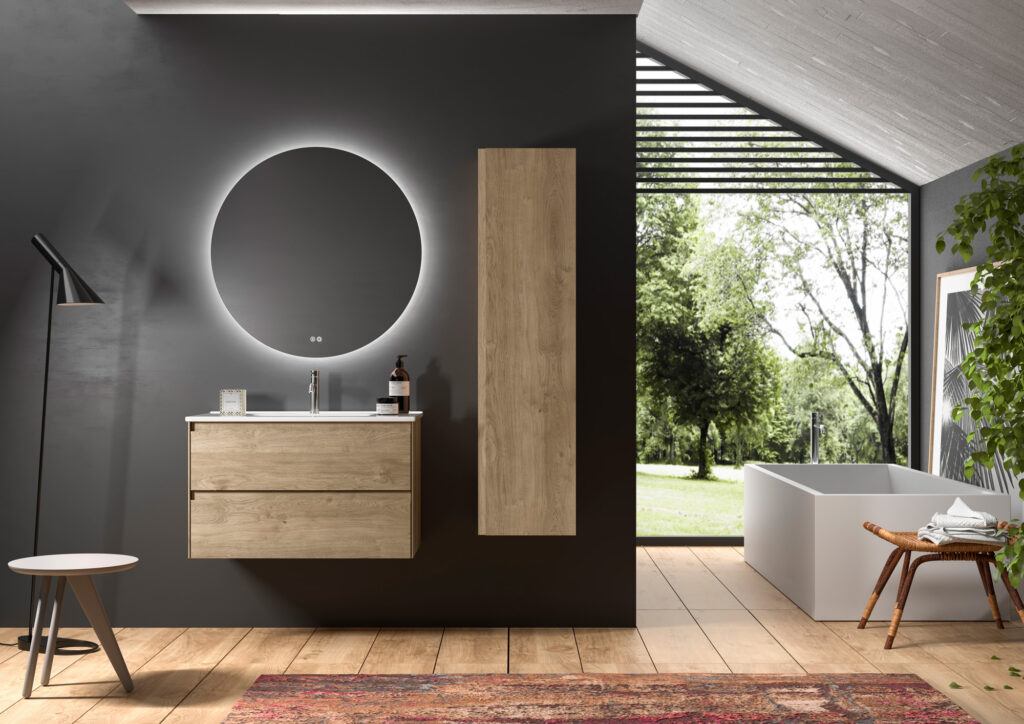 Oak two-drawer vanity unit beneath a round backlit mirror in a dark-walled bathroom with garden view